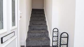 A staircase with carpeted steps leading to an upper floor, a door with a glass panel, and a metal handrail on the right.
