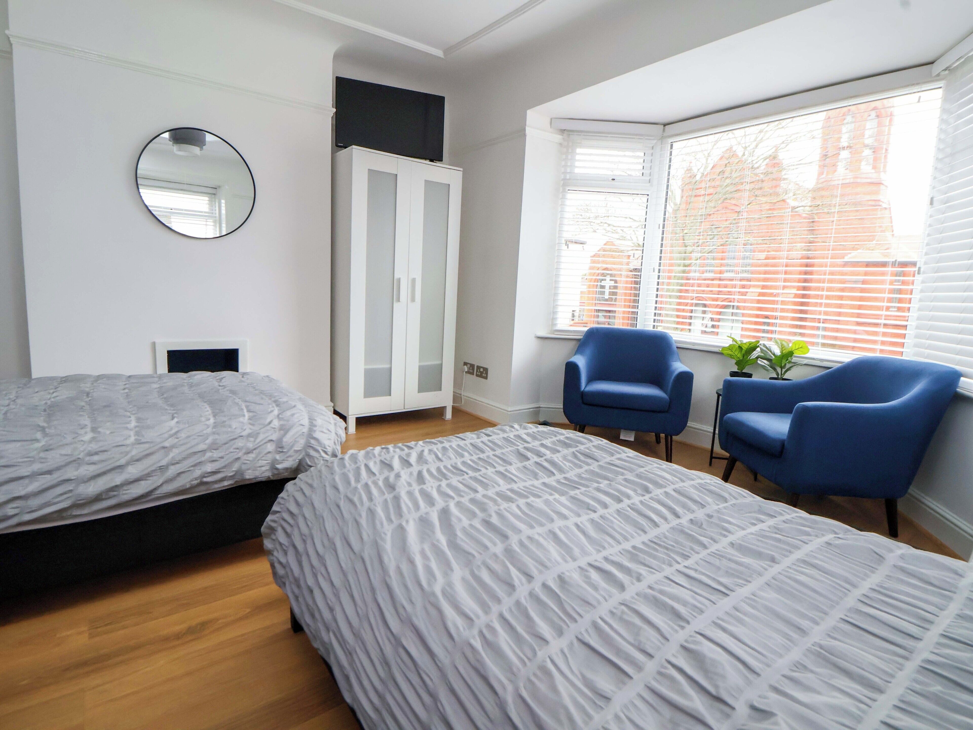 A bedroom with two beds, a wardrobe, a mirror, and a window with blinds.