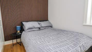 A bedroom with a bed, a nightstand, a lamp, and a window.
