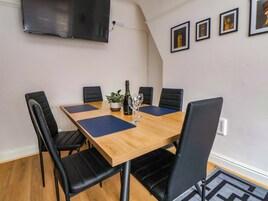 Uma sala de conferências com uma mesa de madeira, cadeiras pretas, um vaso de planta, uma garrafa de vinho e um copo.