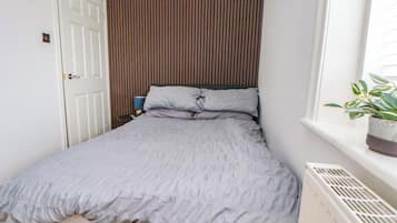 A bedroom with a bed, a wall-mounted radiator, a door, and a window with a plant.