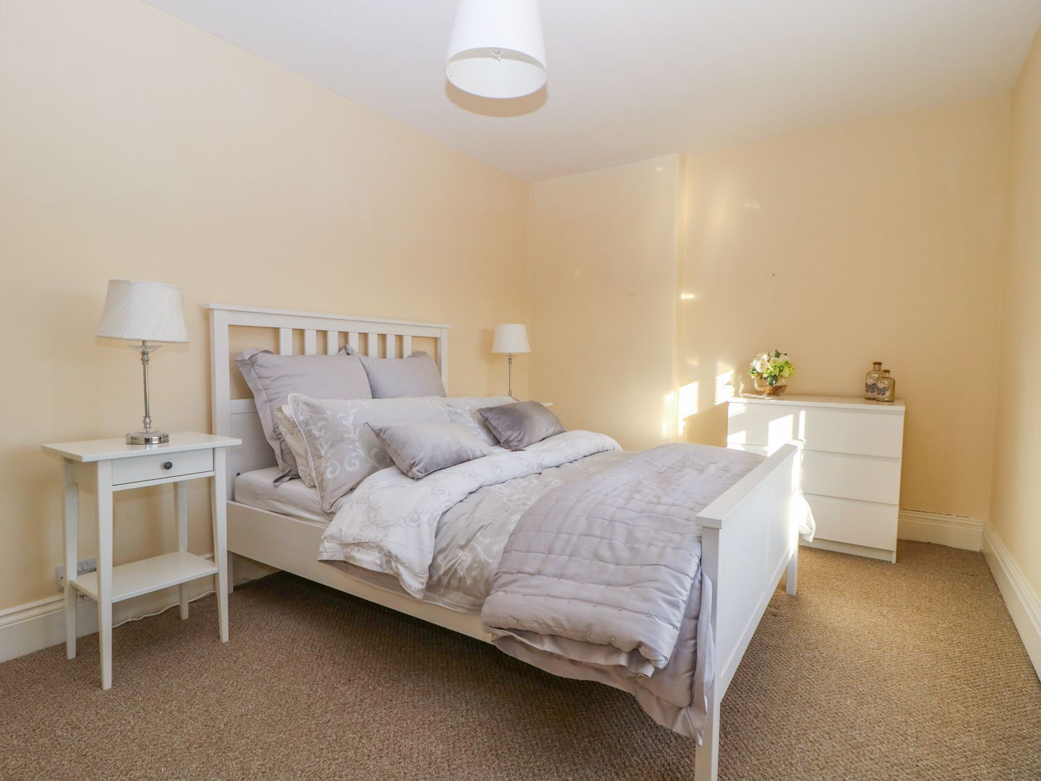 Un dormitorio ordenado con cama, mesitas de noche y cómoda.