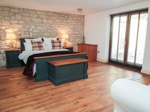 Une chambre avec un mur en pierre, un plancher en bois, un lit avec des oreillers, deux lampes de chevet, un banc et une fenêtre avec des stores.