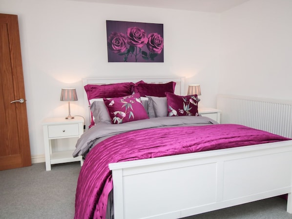 A bedroom with a white bed, purple bedding, and floral pillows. - Tuft House (York)