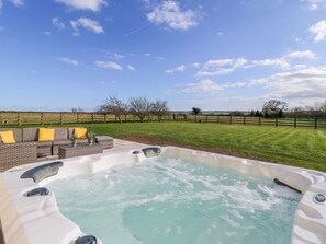 Un bain à remous entouré d’une pelouse verdoyante, d’une clôture en bois et sous un ciel dégagé.