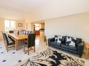 A dining area with a long table and chairs, a black leather sofa with a cow print pillow, and a patterned rug. - Tuft House (York)