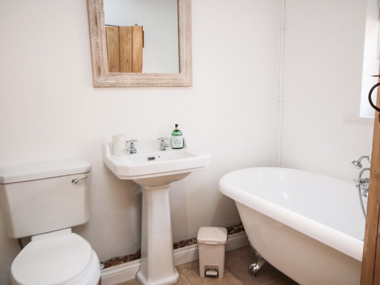 Un baño con inodoro, lavamanos pedestal y bañera independiente.