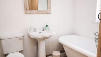 Un baño con inodoro, lavamanos pedestal y bañera independiente.