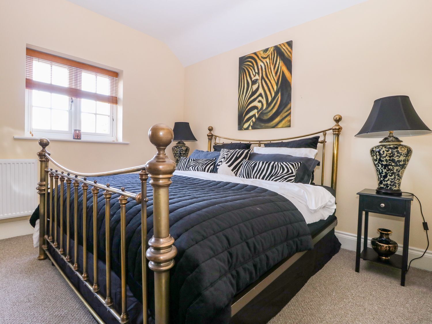 A bedroom with a bed, a window, a painting, a lamp, and a nightstand.