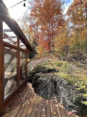 Una cabaña de madera con amplios ventanales, una terraza de madera y vistas del follaje otoñal.