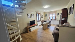 Un vaste espace de vie doté d’un plancher en bois, d’un escalier, d’un coin repas avec une cuisine en arrière-plan et d’un canapé.