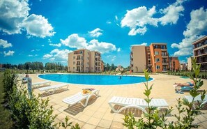 A swimming pool surrounded by lounge chairs and multi-story buildings. - Pool View 2 Bed at Holiday Fort Club (Nessebar)