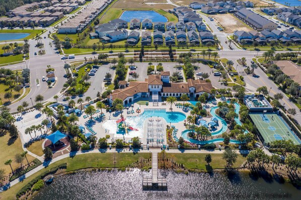 An aerial view of a residential community with a central swimming pool, tennis courts, and a dock extending into a body of water. - Spacious 9-bedroom house in serene Kissimmee with AC (Kissimmee)