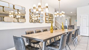 A modern dining area with a wooden table, black leather chairs, and gold-framed mirrors on the wall. - Spacious 9-bedroom house in serene Kissimmee with AC (Kissimmee)