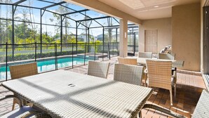 A covered outdoor area with a pool, wicker furniture, and a glass enclosure. - Spacious 9-bedroom house in serene Kissimmee with AC (Kissimmee)