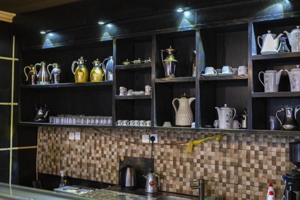 A kitchen with shelves of kitchenware, a tiled backsplash, and a coffee machine.