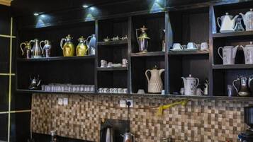 A kitchen with shelves of kitchenware, a tiled backsplash, and a coffee machine.