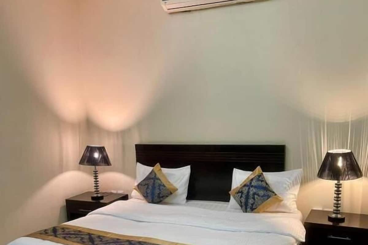A hotel room with a large bed, two bedside tables, an air conditioning unit, and a TV.
