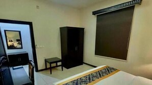 A hotel room with a bed, a desk, a chair, a wardrobe, and a window with blinds. - Quiet Rooms 8  (Riyadh)