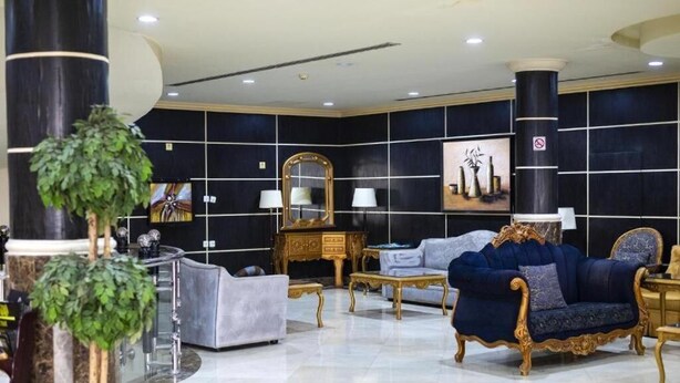 A luxurious lobby with a dark tiled wall, a large mirror, a blue sofa, and a potted plant. - Quiet Rooms 8  (Riyadh)