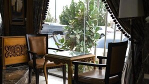 A room with a glass-top table, two chairs, a decorative wooden panel, and a view of parked cars and greenery outside. - Quiet Rooms 8  (Riyadh)