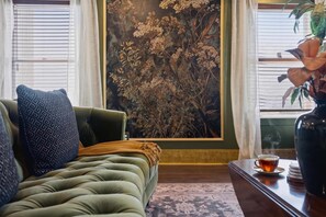 A green sofa with a patterned pillow, a small table with a cup and saucer, and a large botanical print on the wall. - The Bavarian Inn 6 Chic 1 BDR (Covington)