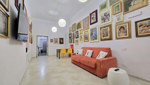 Ein Wohnzimmer mit einer Couch, einem Esstisch mit Stühlen und einem an der Wand montierten Fernseher.