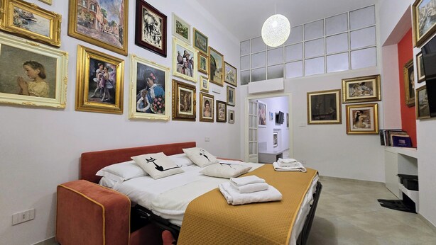 Ein Hotelzimmer mit Bett, Kissen, einem roten Kopfteil, einem großen Fenster und einer Wand mit gerahmten Bildern.