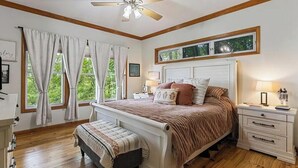 Un dormitorio con cama, mesitas de noche, ventilador de techo y ventana con cortinas.