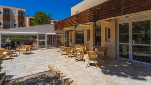 An outdoor patio with wicker furniture, a covered seating area, and a building with large windows and a wooden roof. - 4-guest AC Apartment Near Beach (La Londe-les-Maures)