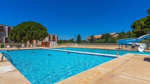 A swimming pool with a slide, surrounded by buildings and trees. - 4-guest AC Apartment Near Beach (La Londe-les-Maures)