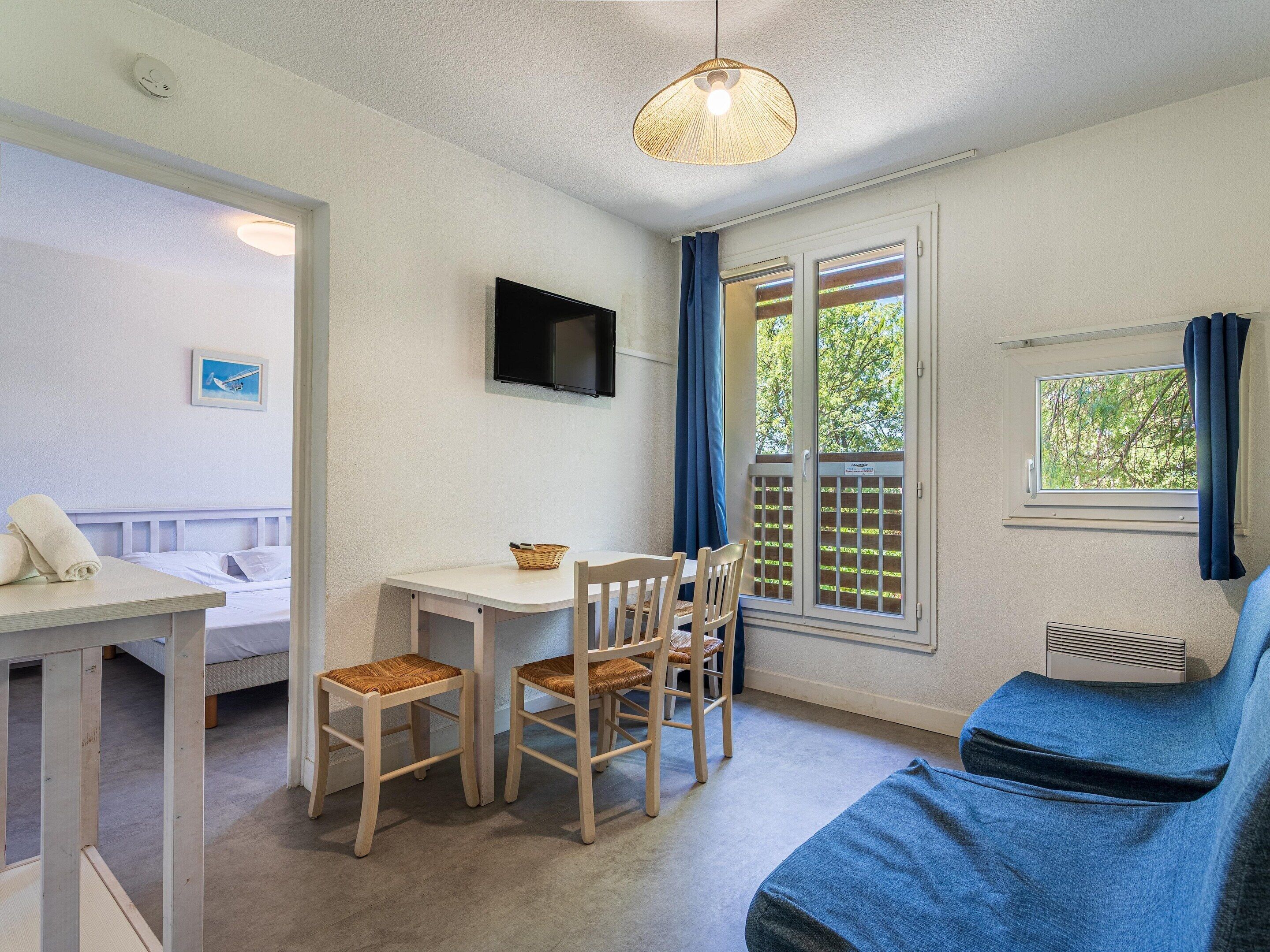 Una habitación con una cama, una mesa con sillas, un televisor y una ventana con cortinas.
