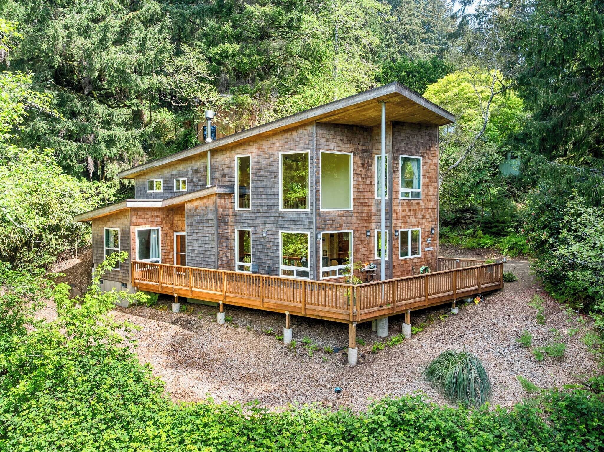 Modern retreat nestled among lush evergreens, featuring a spacious wraparound deck and floor-to-ceiling windows that invite natural light and forest views throughout.