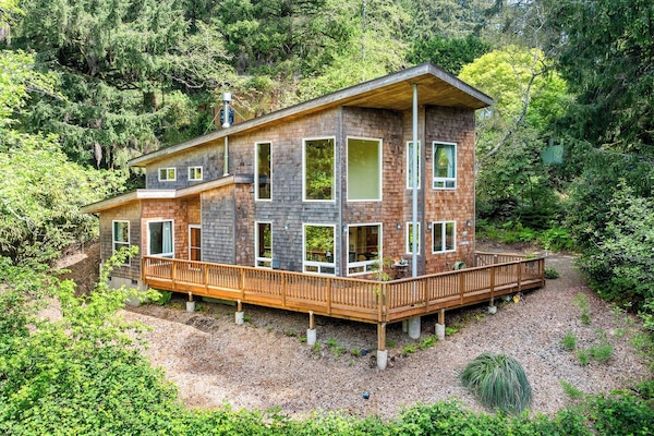 Modern retreat nestled among lush evergreens, featuring a spacious wraparound deck and floor-to-ceiling windows that invite natural light and forest views throughout.