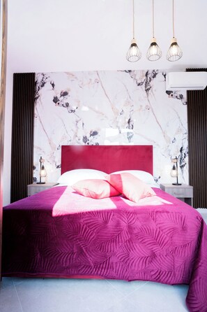 Ein modernes Schlafzimmer mit einem roten Kopfteil, einer Wand im Marmor-Look, einer rosa Bettdecke und Pendelleuchten.