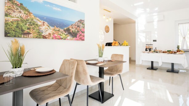A modern dining area with a large scenic painting, a buffet setup, and a clean, bright interior. - Villa Rossa (Agerola)