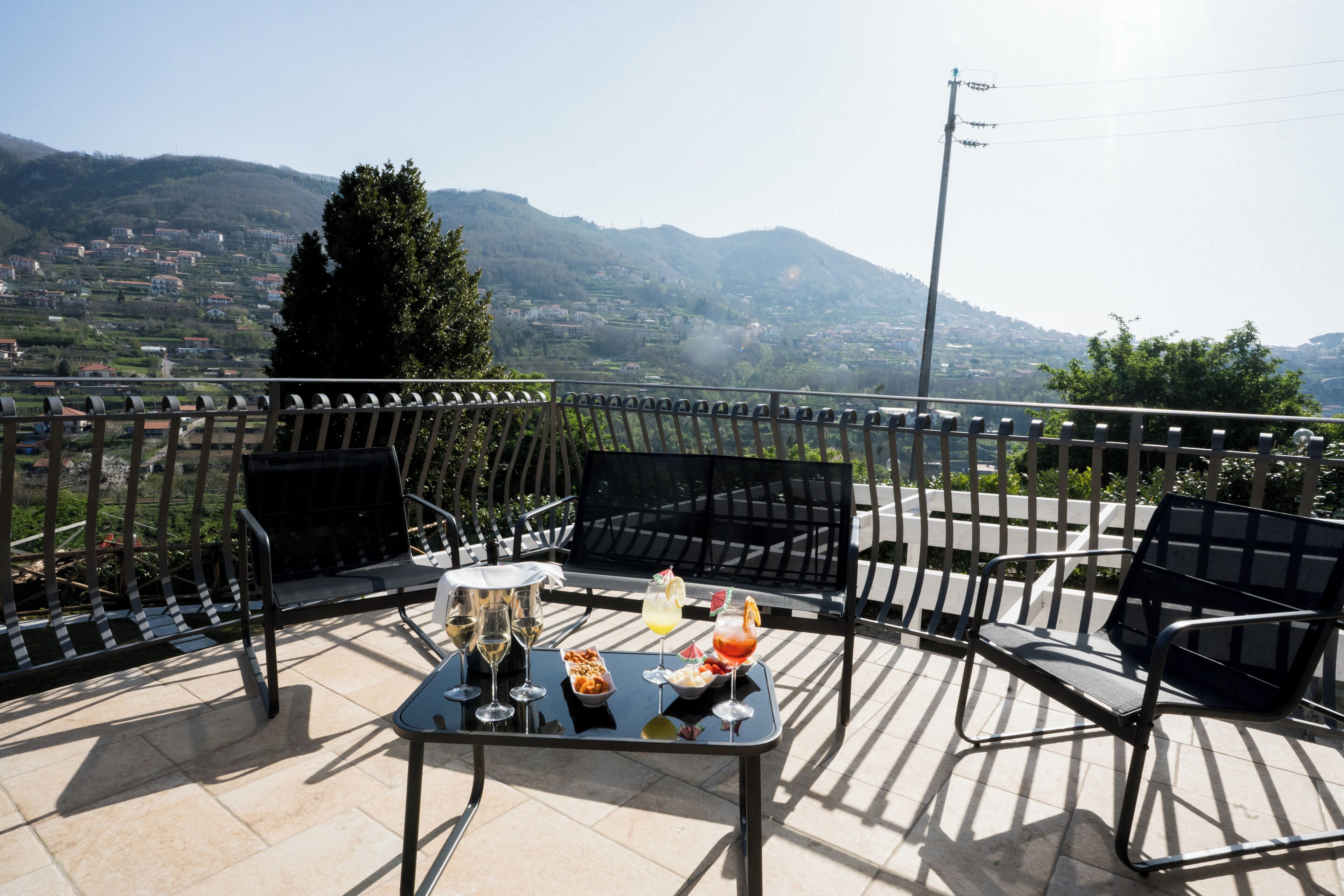 A terrace with a table set for dining, outdoor seating, and a view of a mountainous landscape.