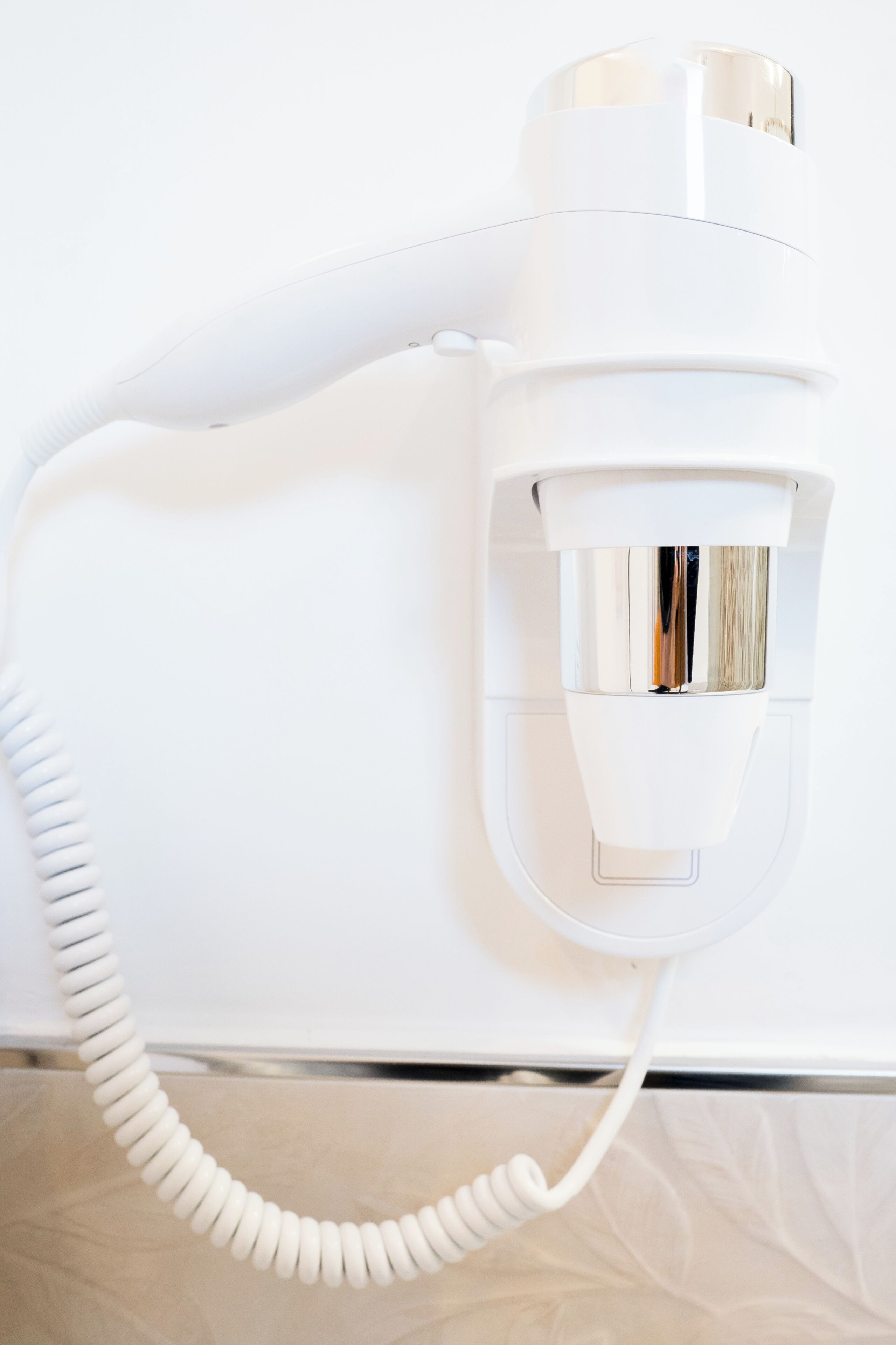 A white hair dryer mounted on a wall with a coiled cord.