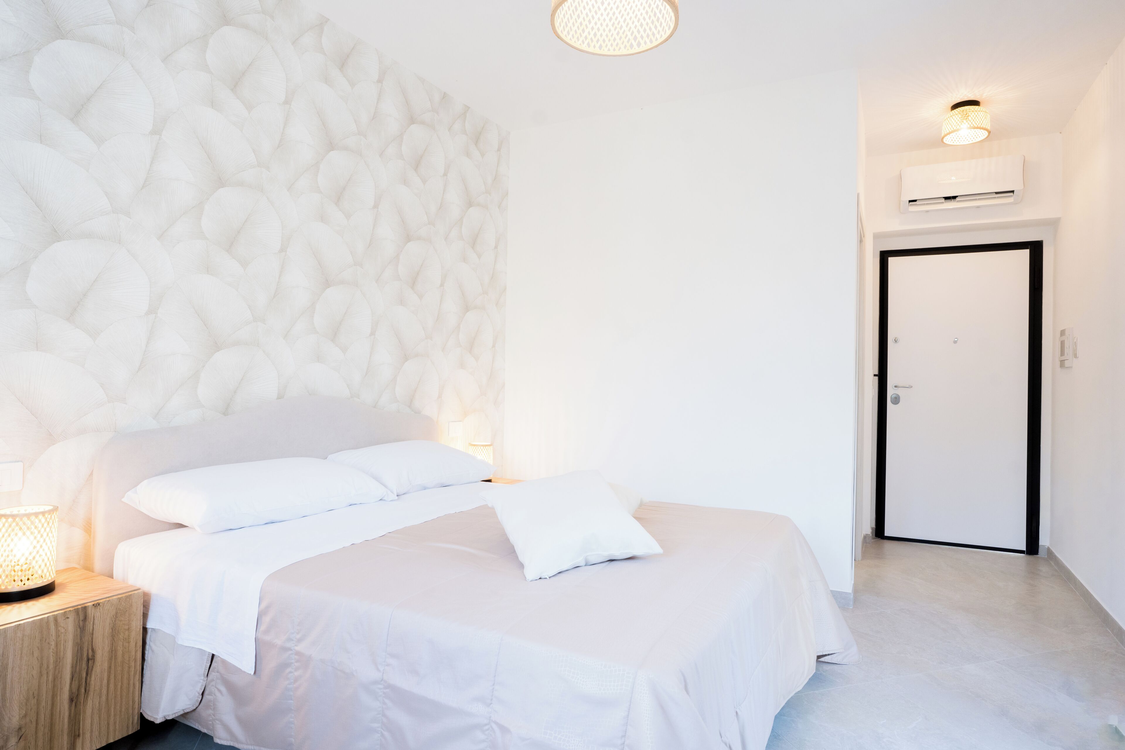 Ein modernes Schlafzimmer mit einer Steinsäule, einem Bett mit weißer Bettwäsche, einem Nachttisch mit Lampe und einer Wand-Klimaanlage.