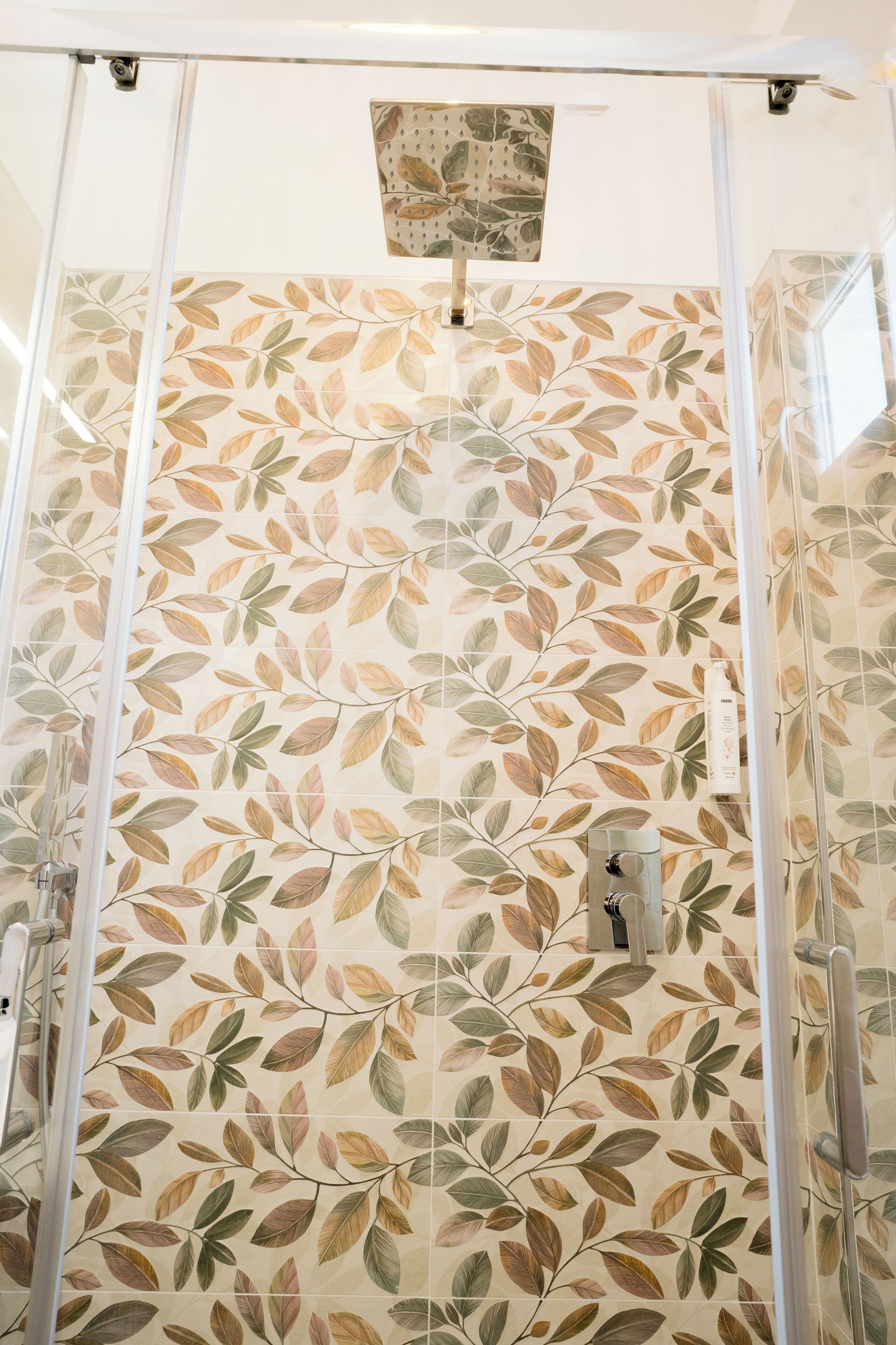 A shower with a leaf-patterned tile wall, a glass enclosure, and a visible water control knob.