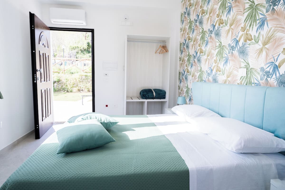 Une chambre à coucher comprenant un lit, une armoire, un portant et donnant sur l’extérieur.