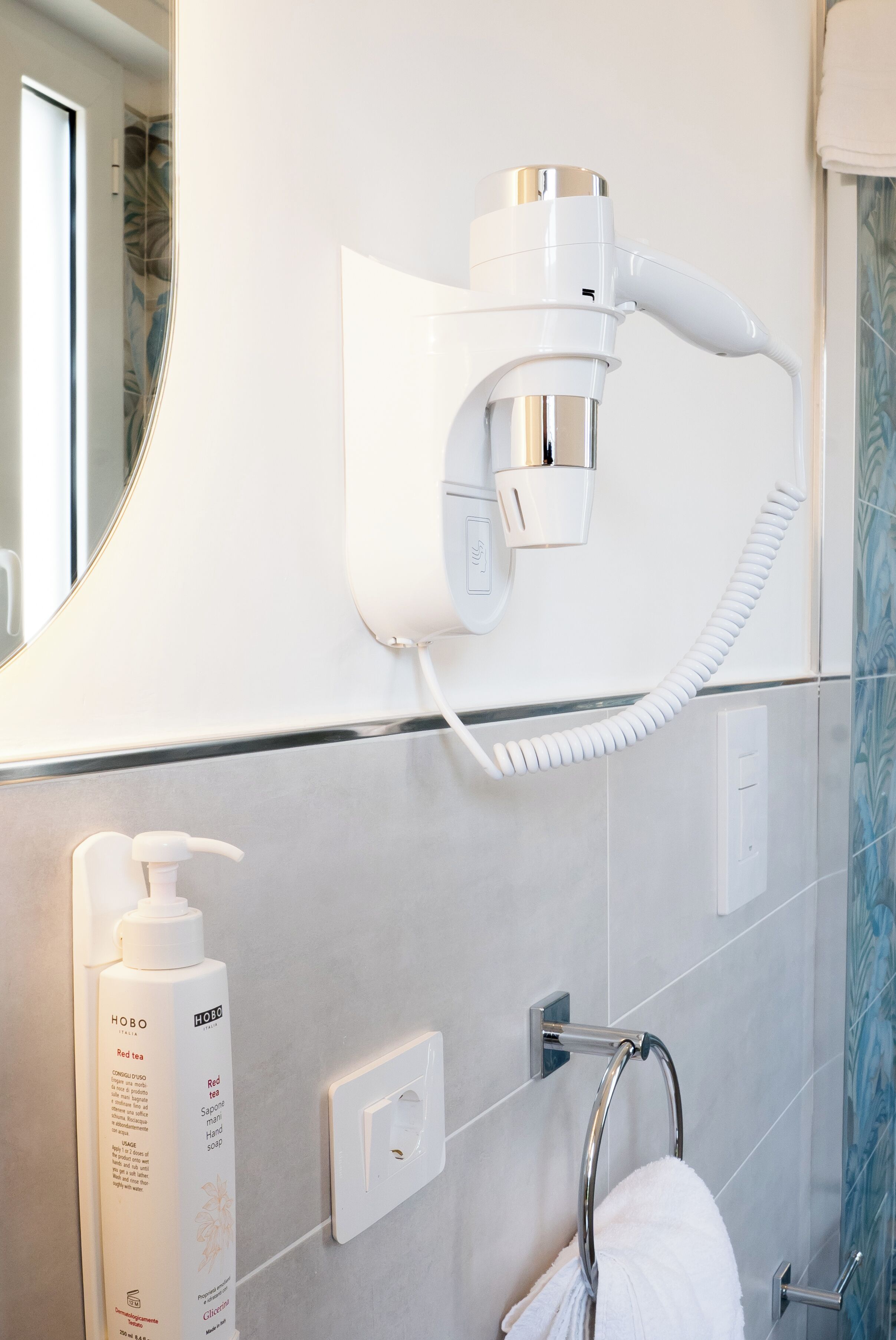 A bathroom with a hairdryer mounted on the wall, a towel rack, a bottle of red tea, and a light switch.