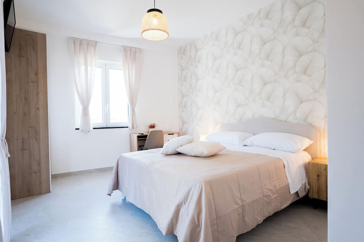 Une chambre à coucher comprenant un lit, un bureau, une chaise, une armoire en bois et un mur orné d’un motif texturé.