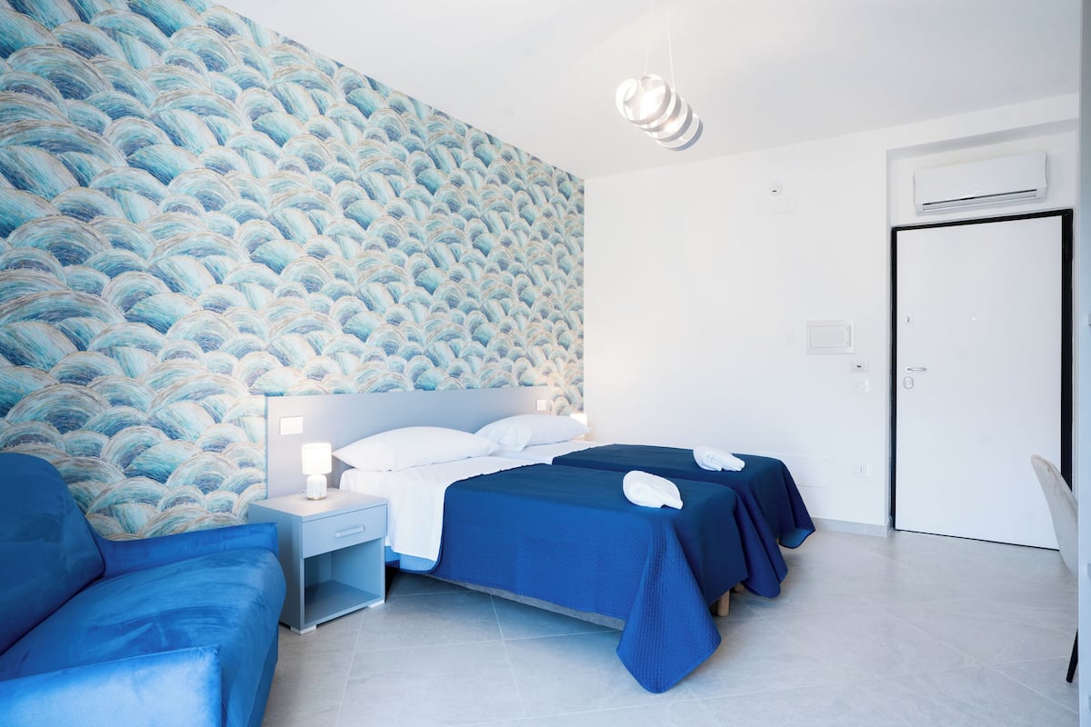 Une chambre d’hôtel avec un mur à motifs, un lit avec une literie bleue, une table de chevet avec une lampe et une chaise.