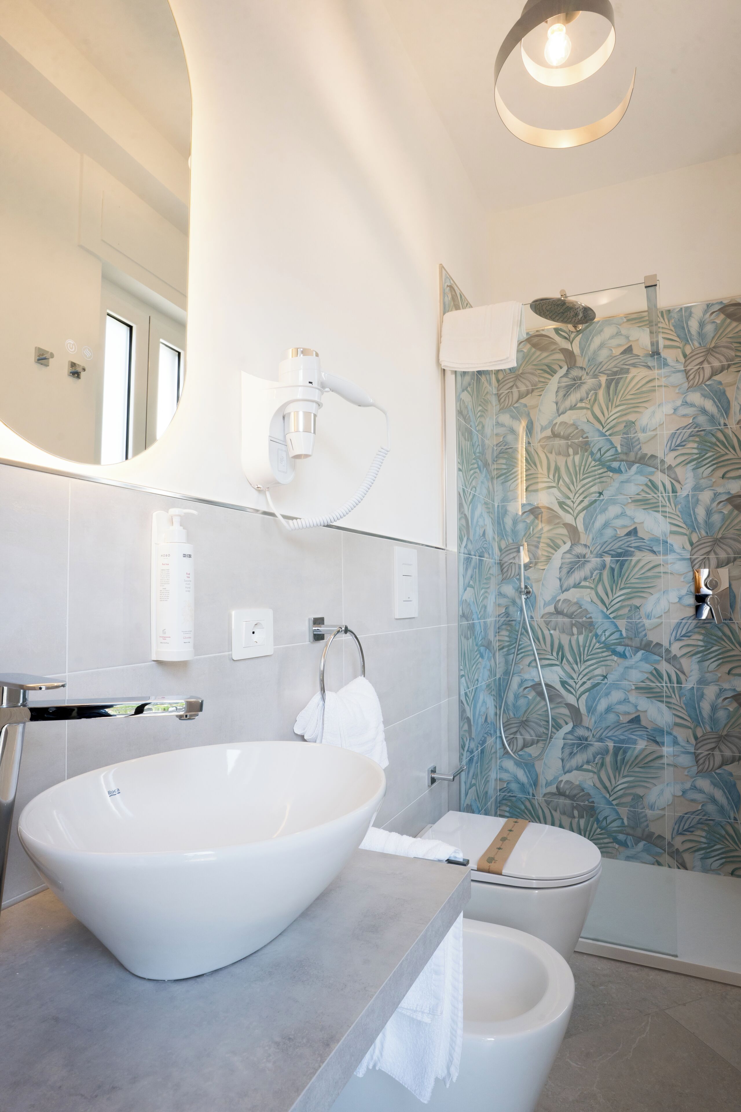 A modern bathroom with a large vessel sink, a toilet, and a shower with floral-patterned glass doors.