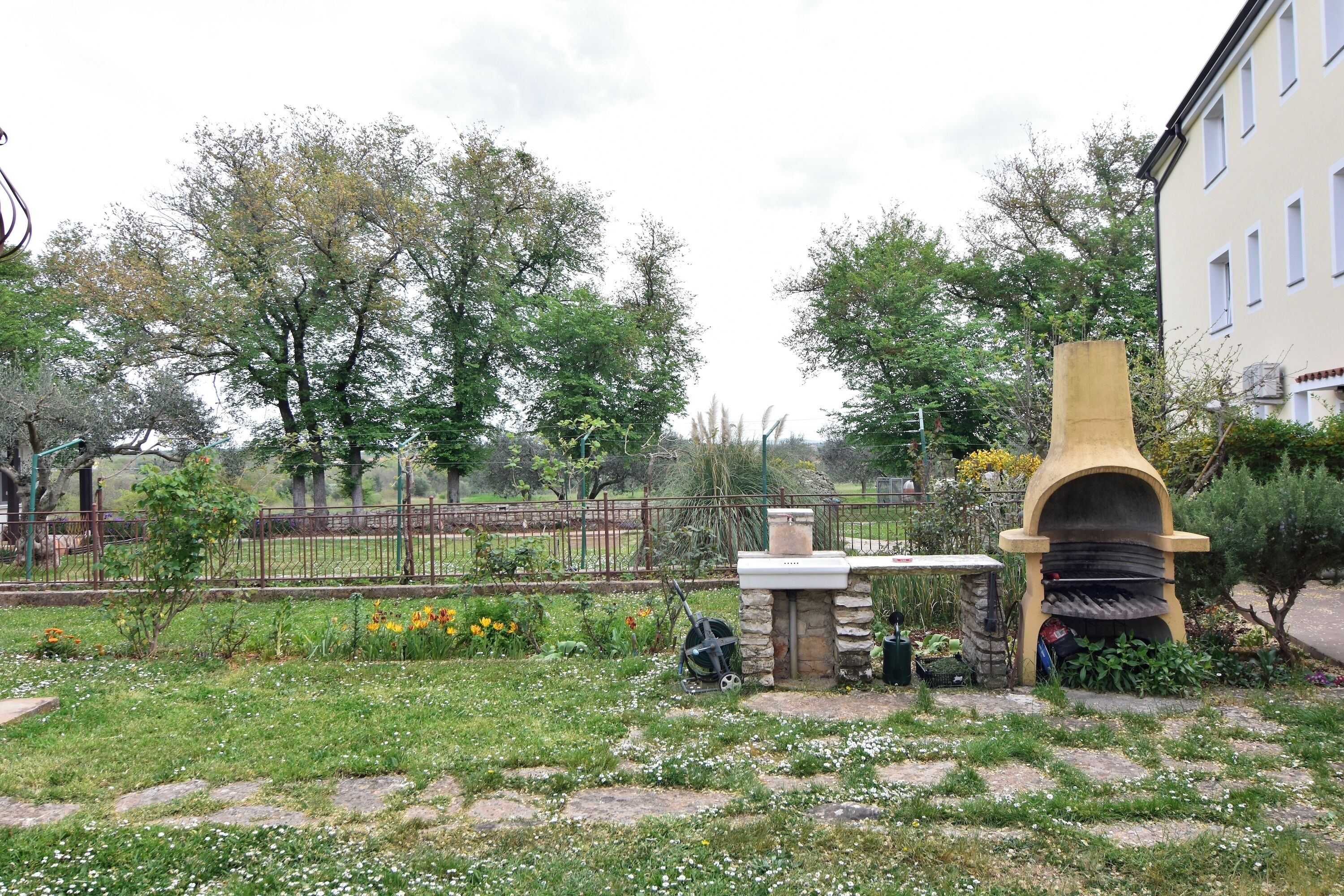 A garden with a stone structure, a metal grill, and a building in the background.