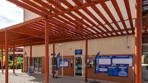 Un espacio al aire libre techado con mostrador de recepción, carteles informativos y piso de baldosas.