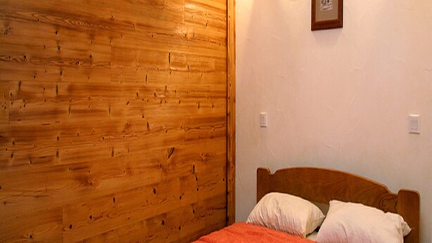 A room with a wooden wall, a bed with a red blanket, and a nightstand with a lamp. - Apartment by the Slopes in Les Deux Alpes (Les Deux Alpes)