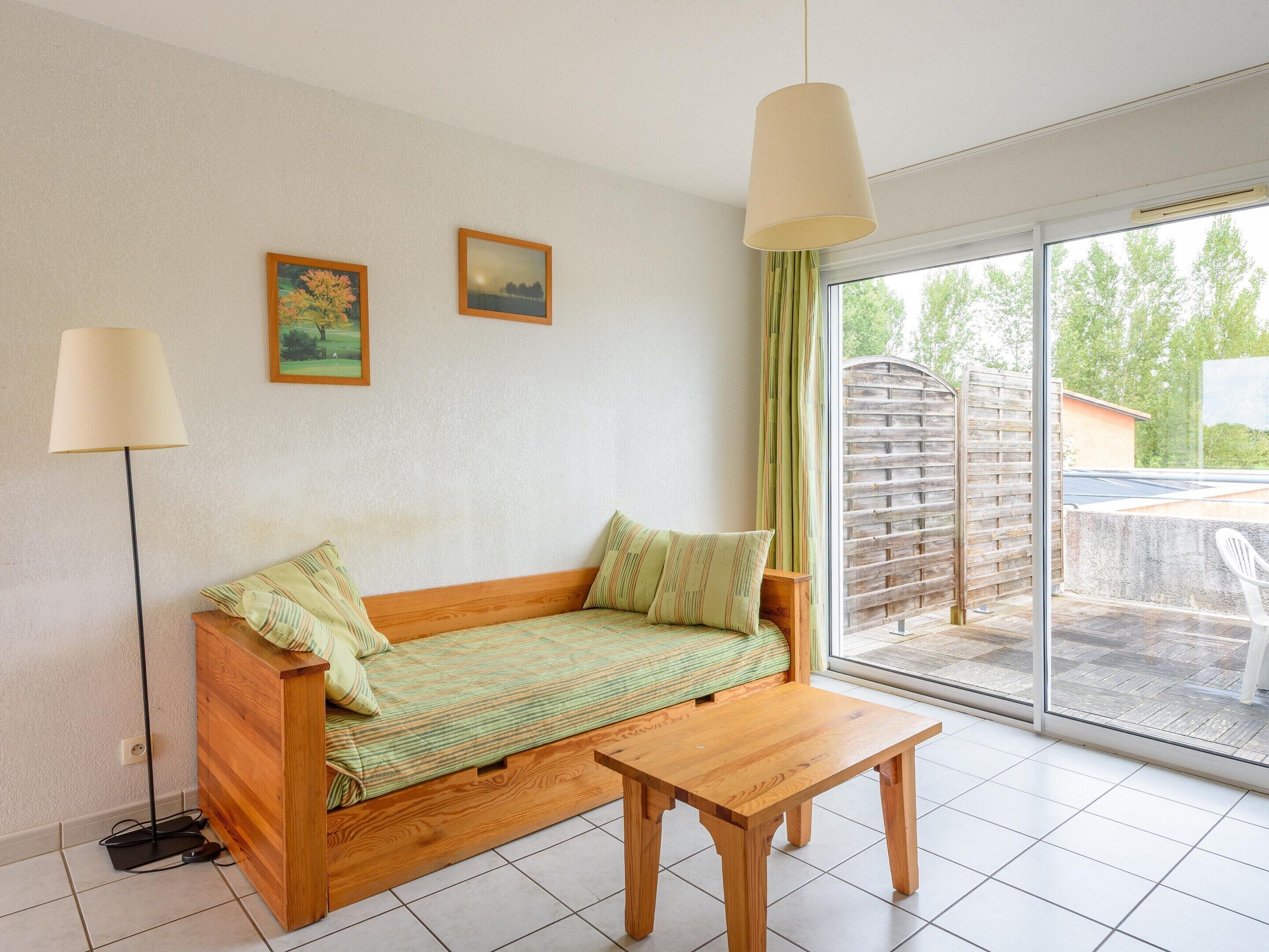 A room with a wooden sofa, a small wooden table, a floor lamp, and a sliding glass door leading to an outdoor area.