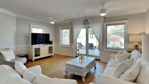 Ett rymligt vardagsrum med vita möbler, en platt-TV och utsikt över den utomhusbelägna uteplatsen.